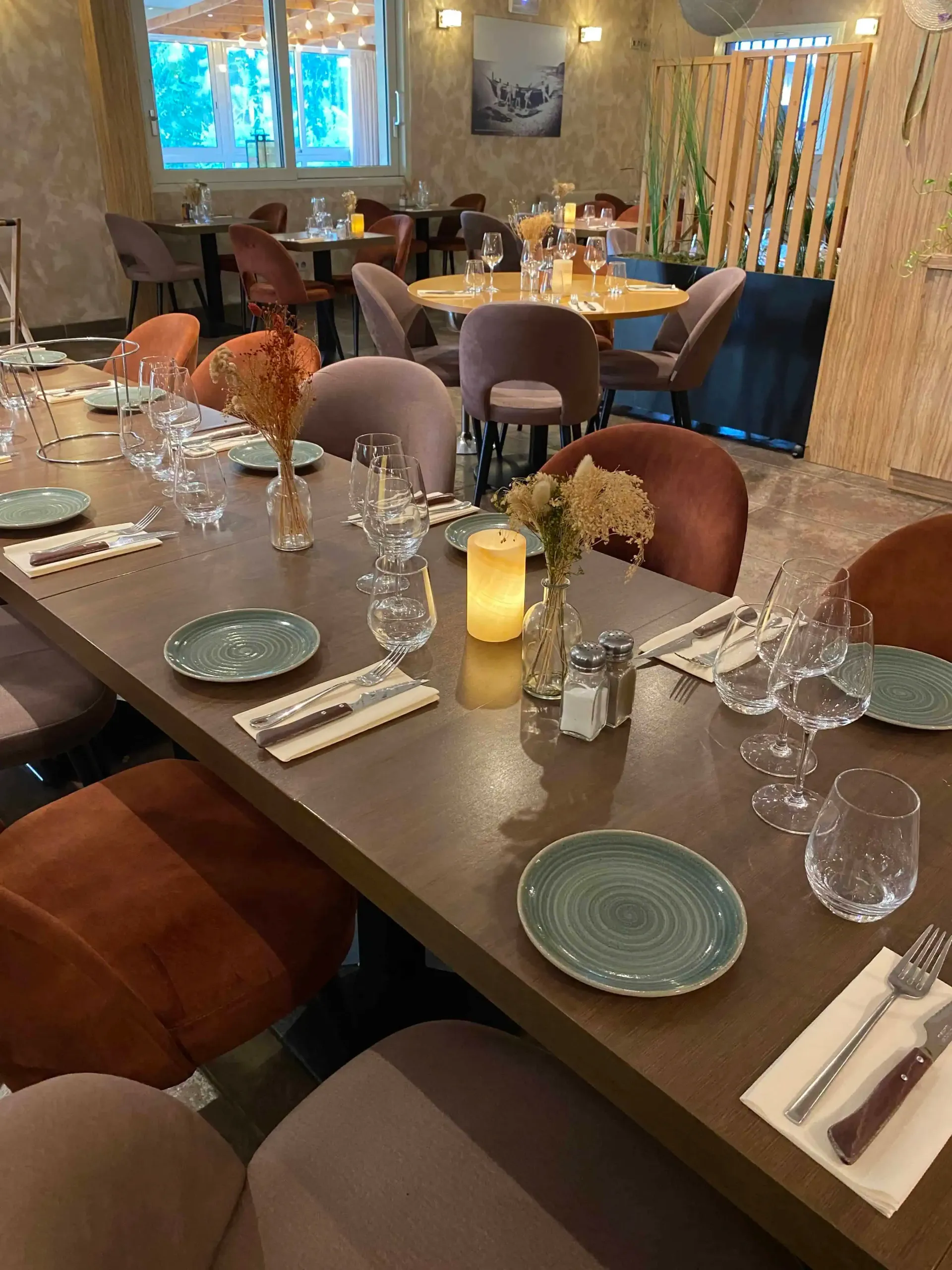 Un restaurant à l'intérieur aménagé avec de longues tables dressées avec des assiettes vertes, des couverts et de petits vases de fleurs.