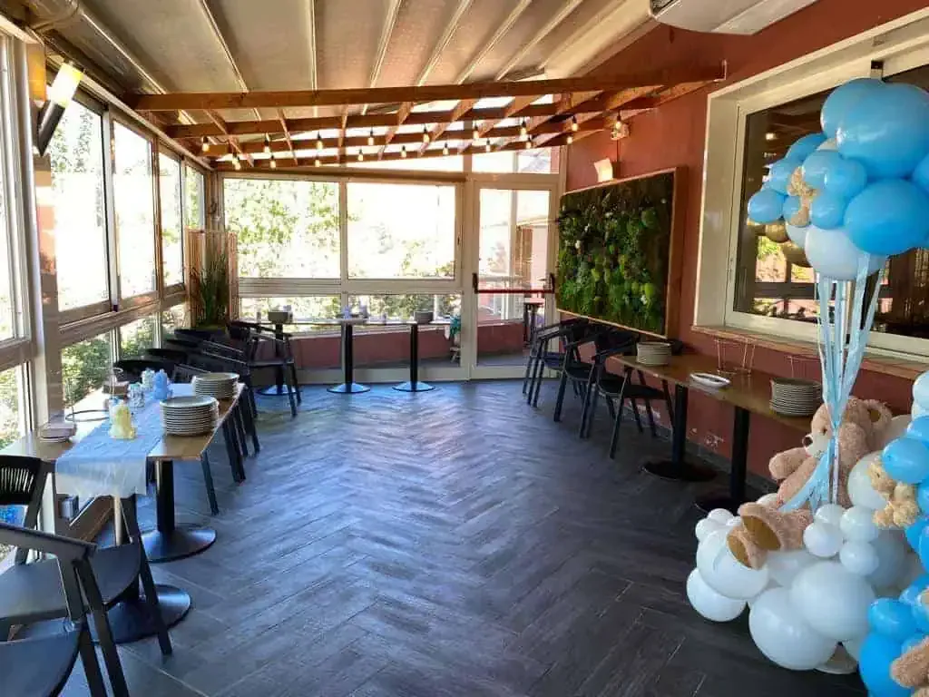 Une terrasse ensoleillée avec des tables dressées pour un événement, ornée d'une grande composition de ballons bleus et blancs.