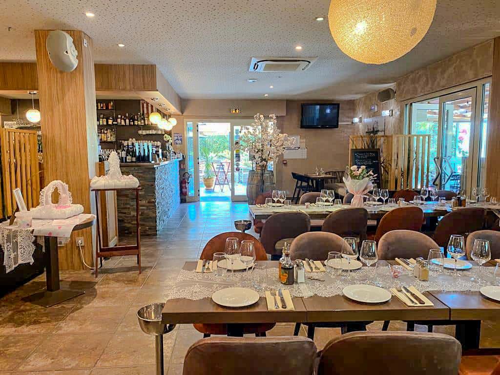 Vue intérieure d'un restaurant avec un décor en bois, des tables dressées pour les repas et un coin bar en arrière-plan.