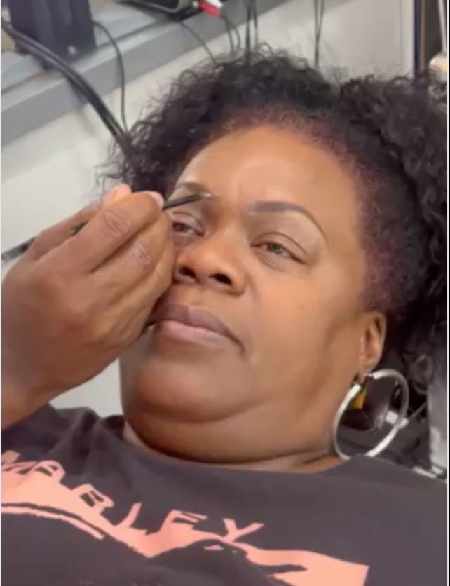 A woman is getting her eyebrows done by a man.