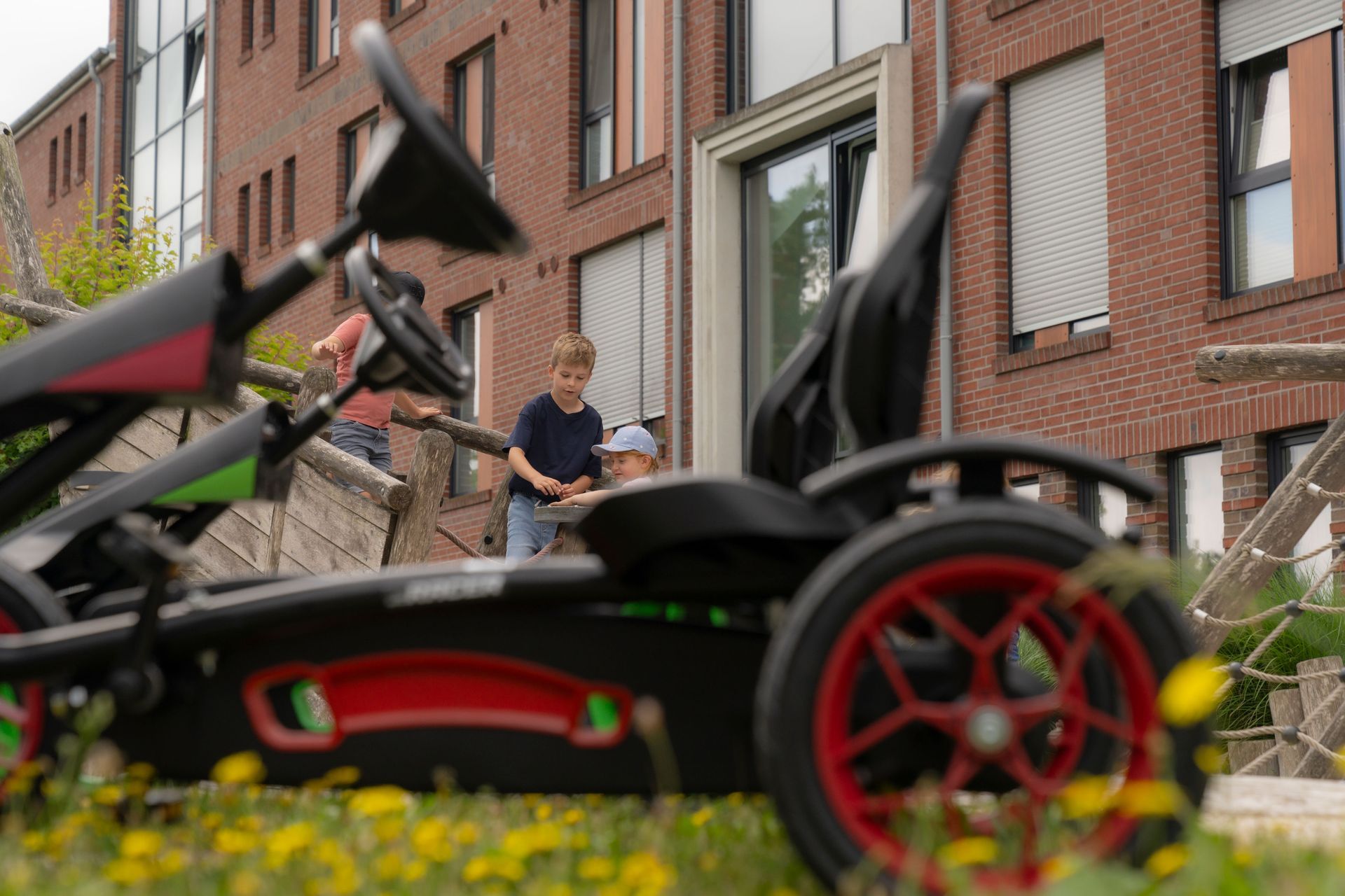 Eine Person schiebt einen Kinderwagen auf einer Stadtstraße; im Hintergrund sind Fahrräder und Backsteingebäude zu sehen.