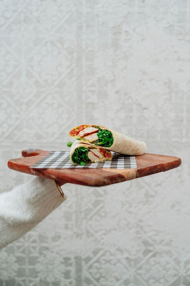 A person is holding a wooden cutting board with a wrap on it.