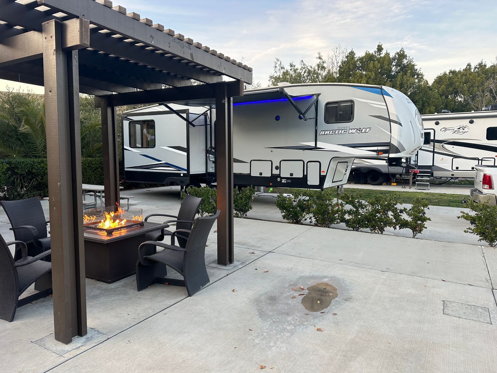 A rv is parked under a pergola next to a fire pit.