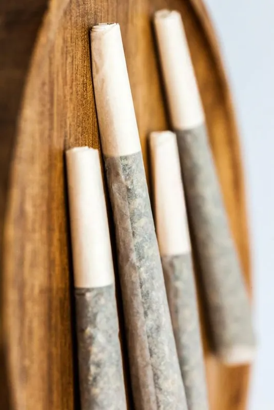 Four rolled joints with white filter tips on a wooden surface.