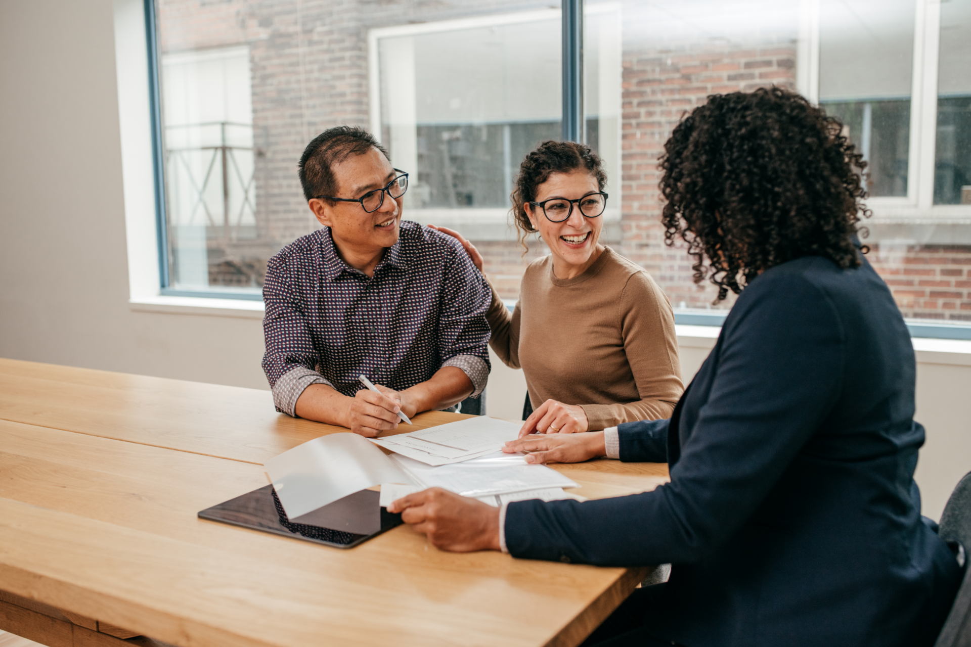 Three coworkers in a meeting at a wooden table, discussing papers in a bright office