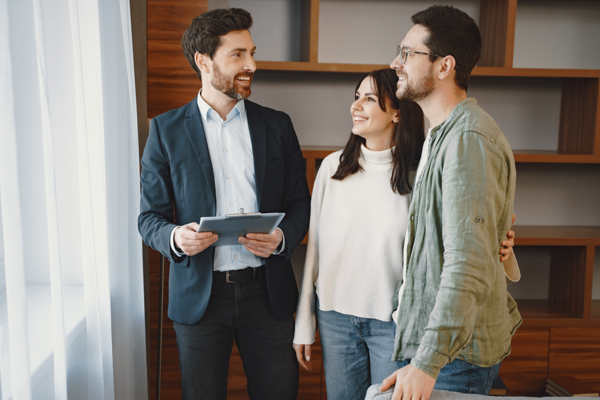 Three people stand in a bright room, smiling and talking with a tablet nearby.