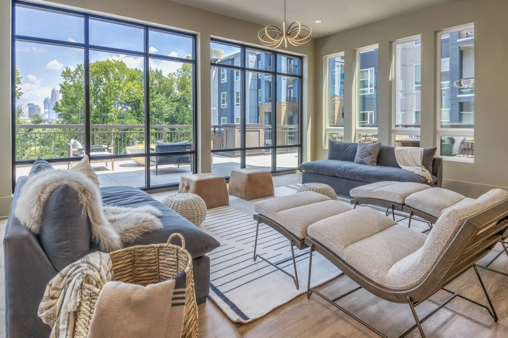 Bright living room with floor-to-ceiling windows and a balcony; gray sofa, lounge chair, and ottomans.