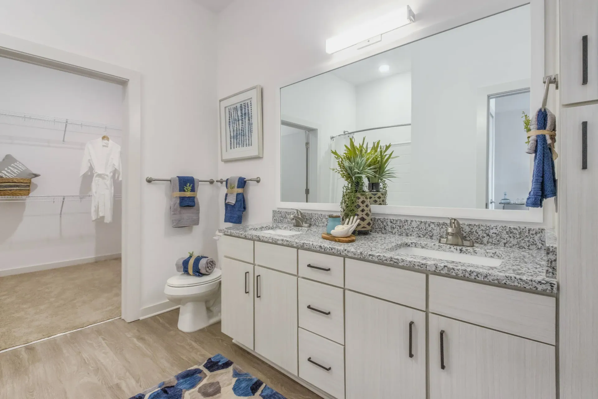 Bright bathroom with a double-sink granite vanity, large mirror, and an open closet area.