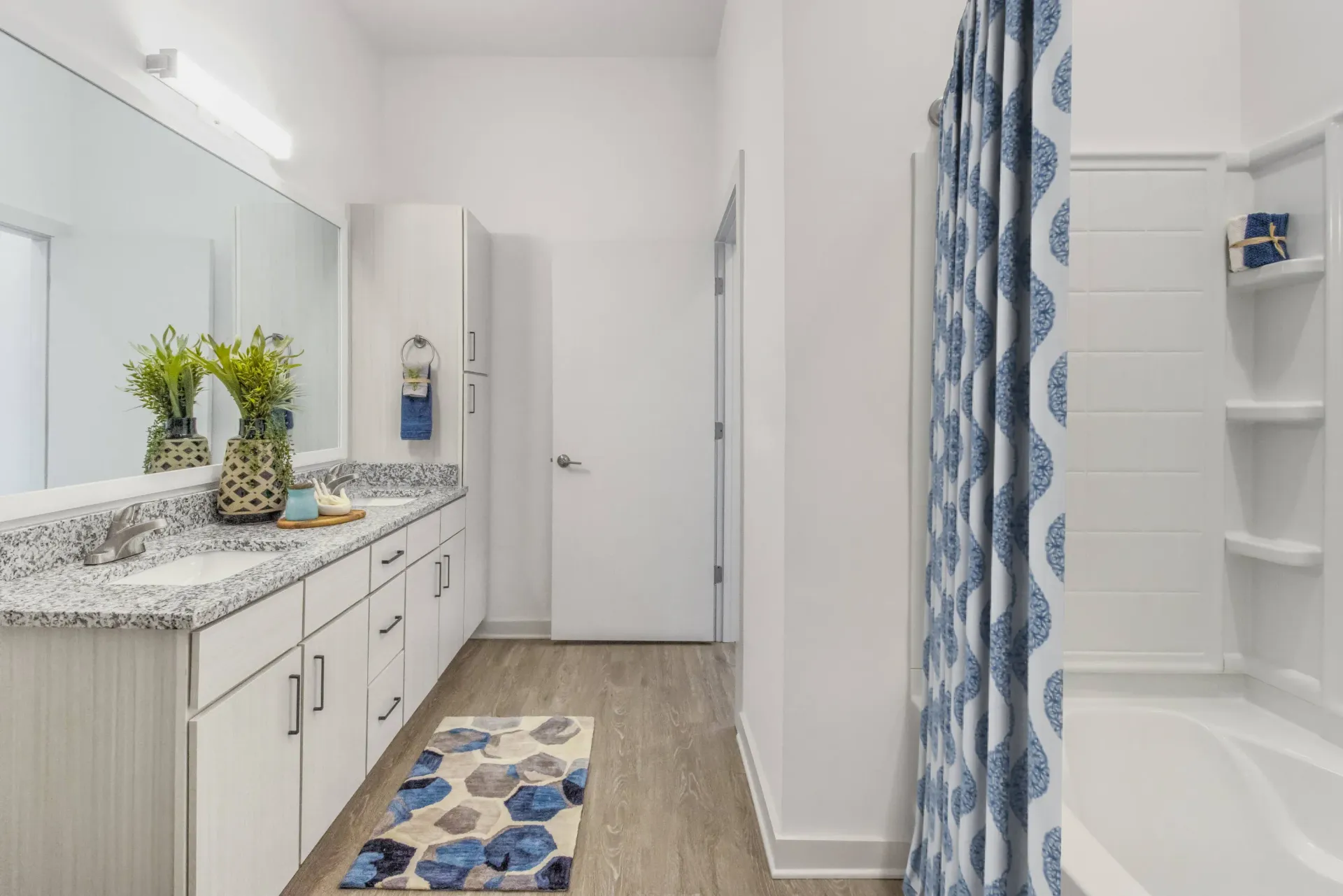 Bright bathroom with a double-sink vanity, granite countertop, and a blue patterned shower curtain.