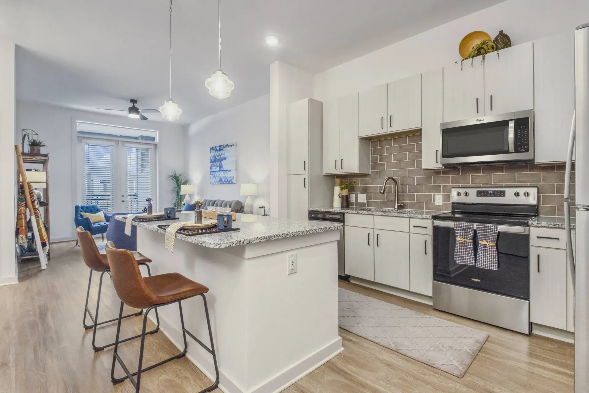 Open-concept kitchen with island, granite countertops, stainless steel appliances, and a living area beyond.