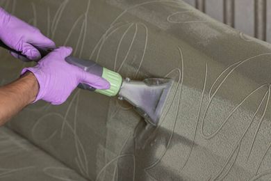A person is cleaning a couch with a vacuum cleaner.