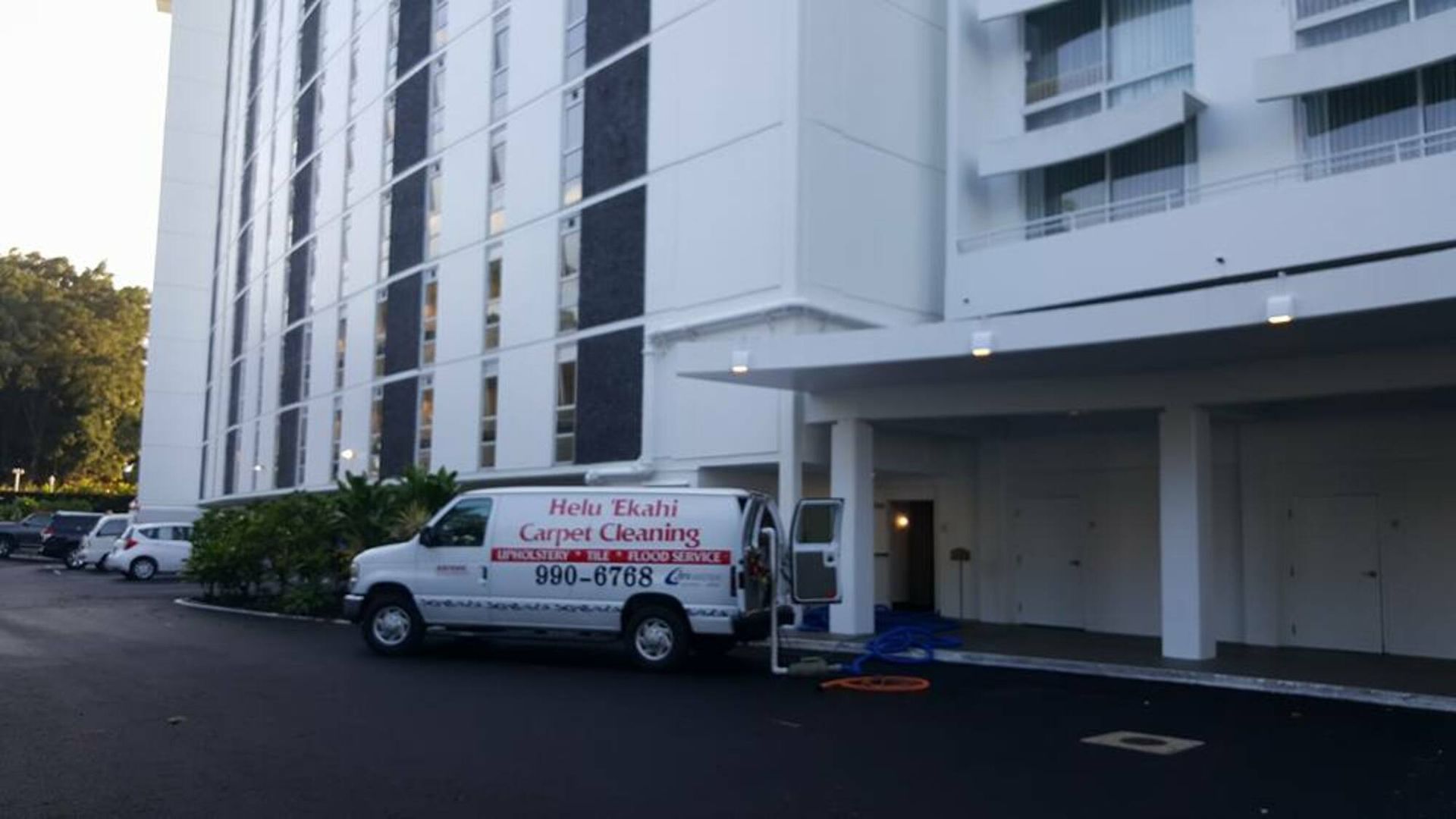A white van is parked in front of a large white building.