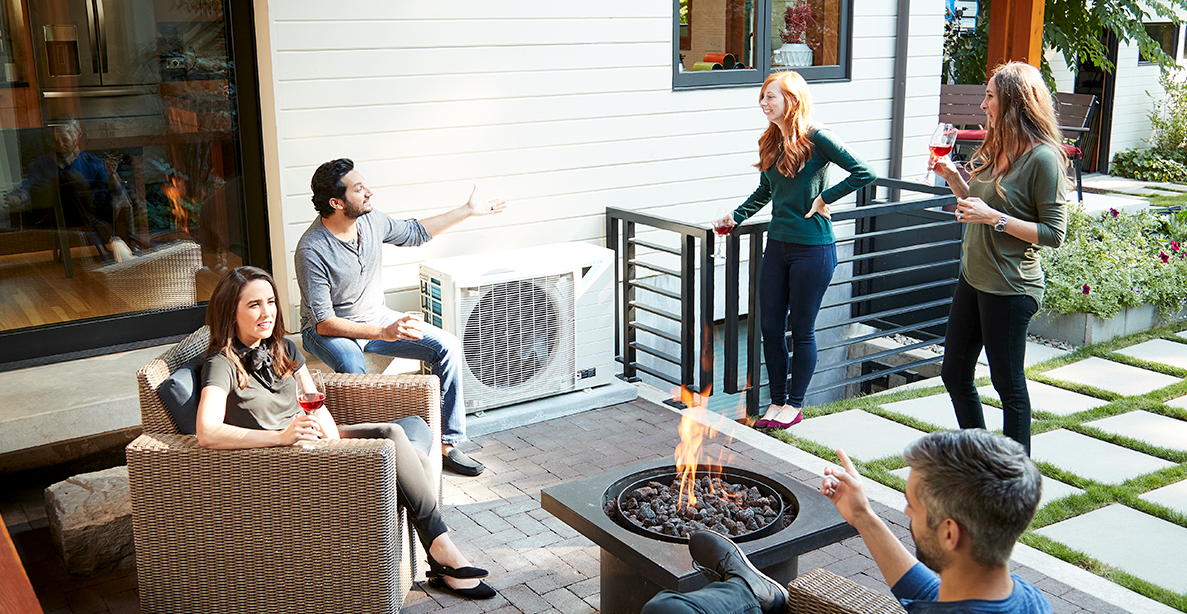 A group of people are sitting around a fire pit on a patio.