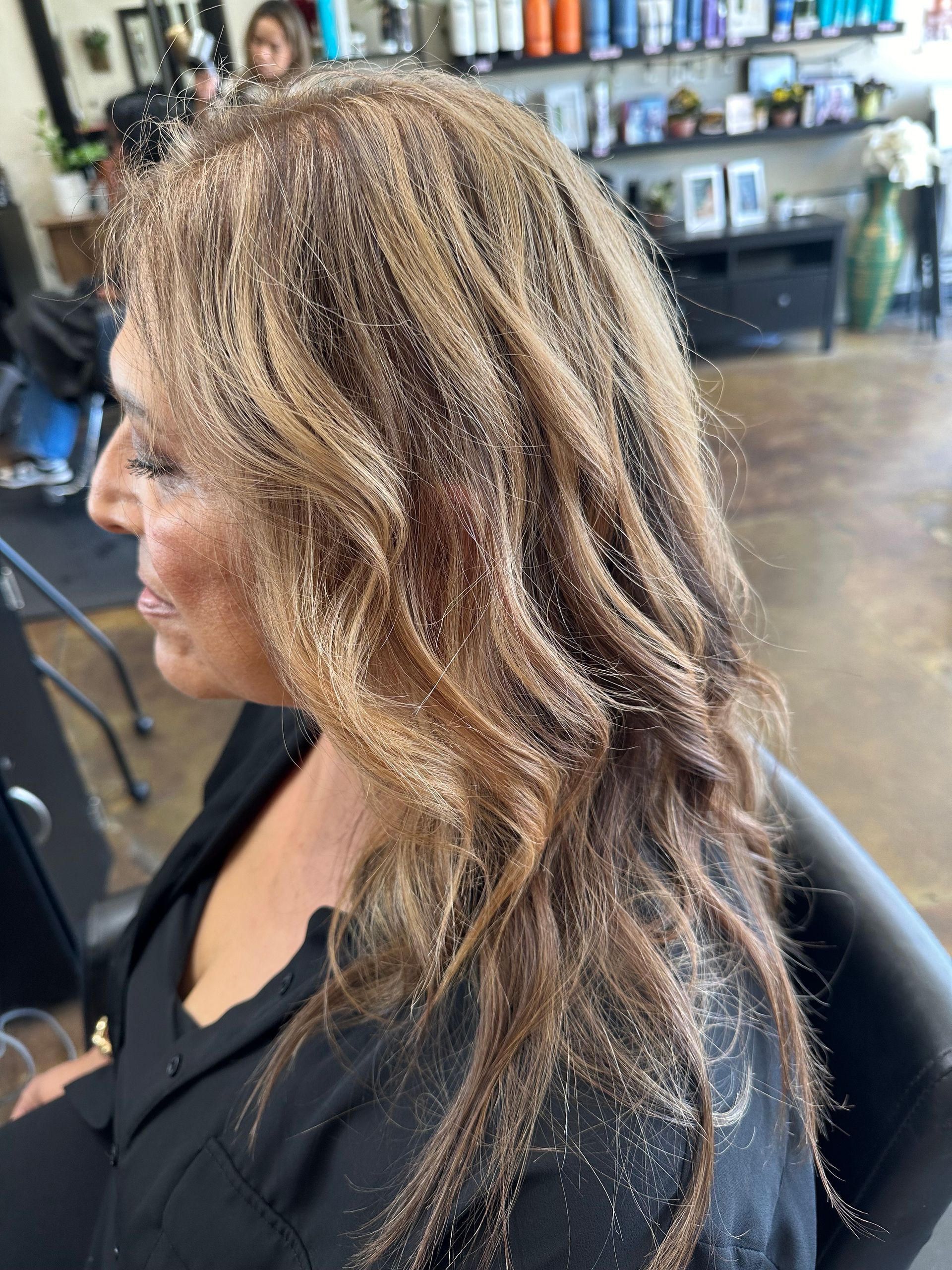 Woman with long, wavy brown hair with blonde highlights in a salon.