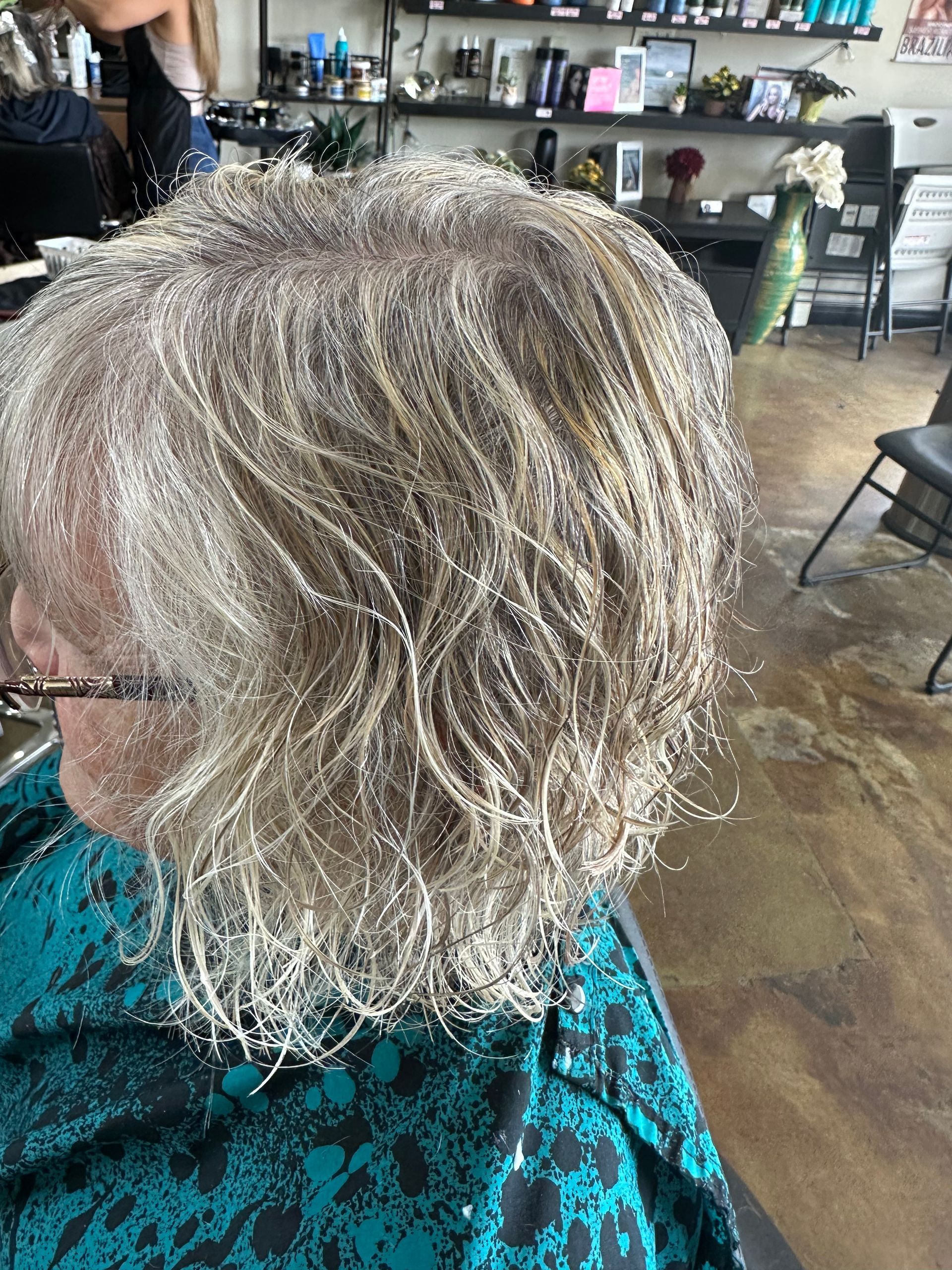 Woman with short, wavy silver hair in a salon, wearing a teal patterned top.
