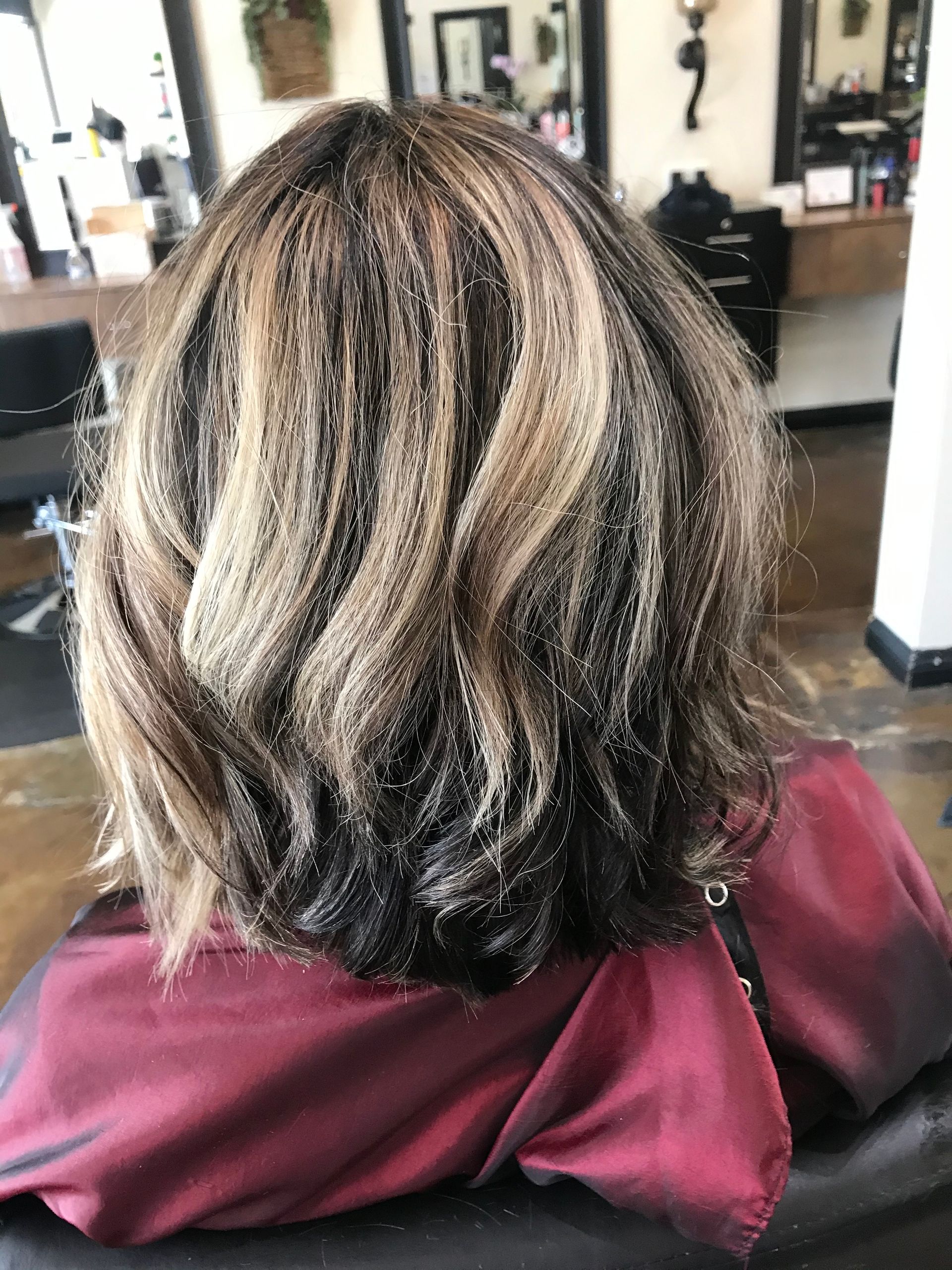 Woman's short, wavy hair with blonde highlights and dark roots, in a salon setting.