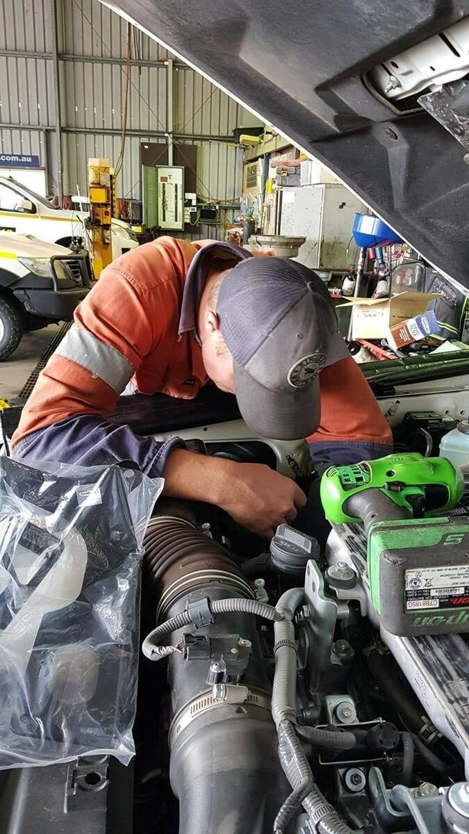 A Man Is Working on The Engine of A Truck in A Garage — Coalfields Mechanical & Towing in Blackwater, QLD