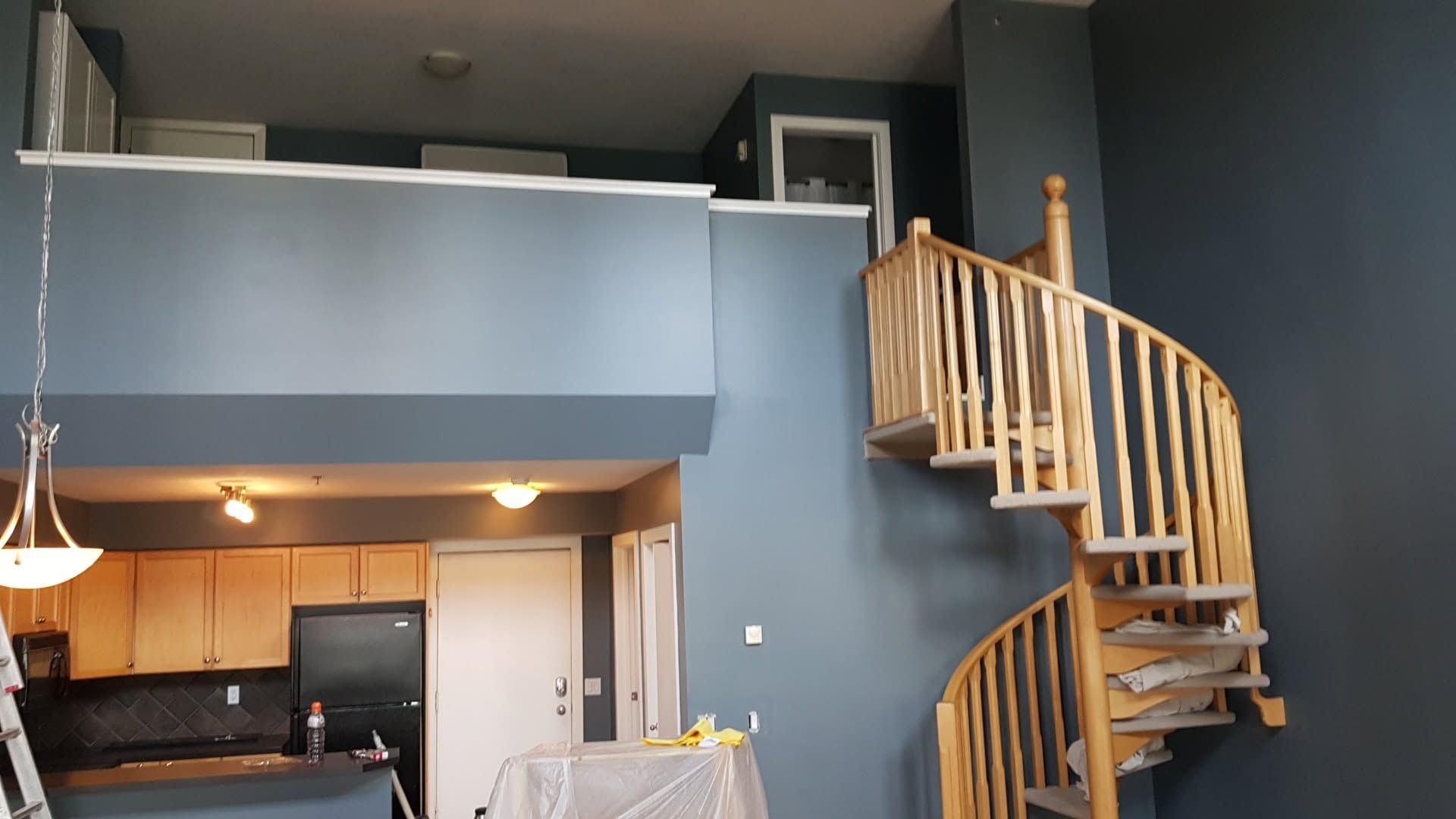 Modern loft interior with blue walls, kitchen below, and a wooden spiral staircase to a mezzanine.