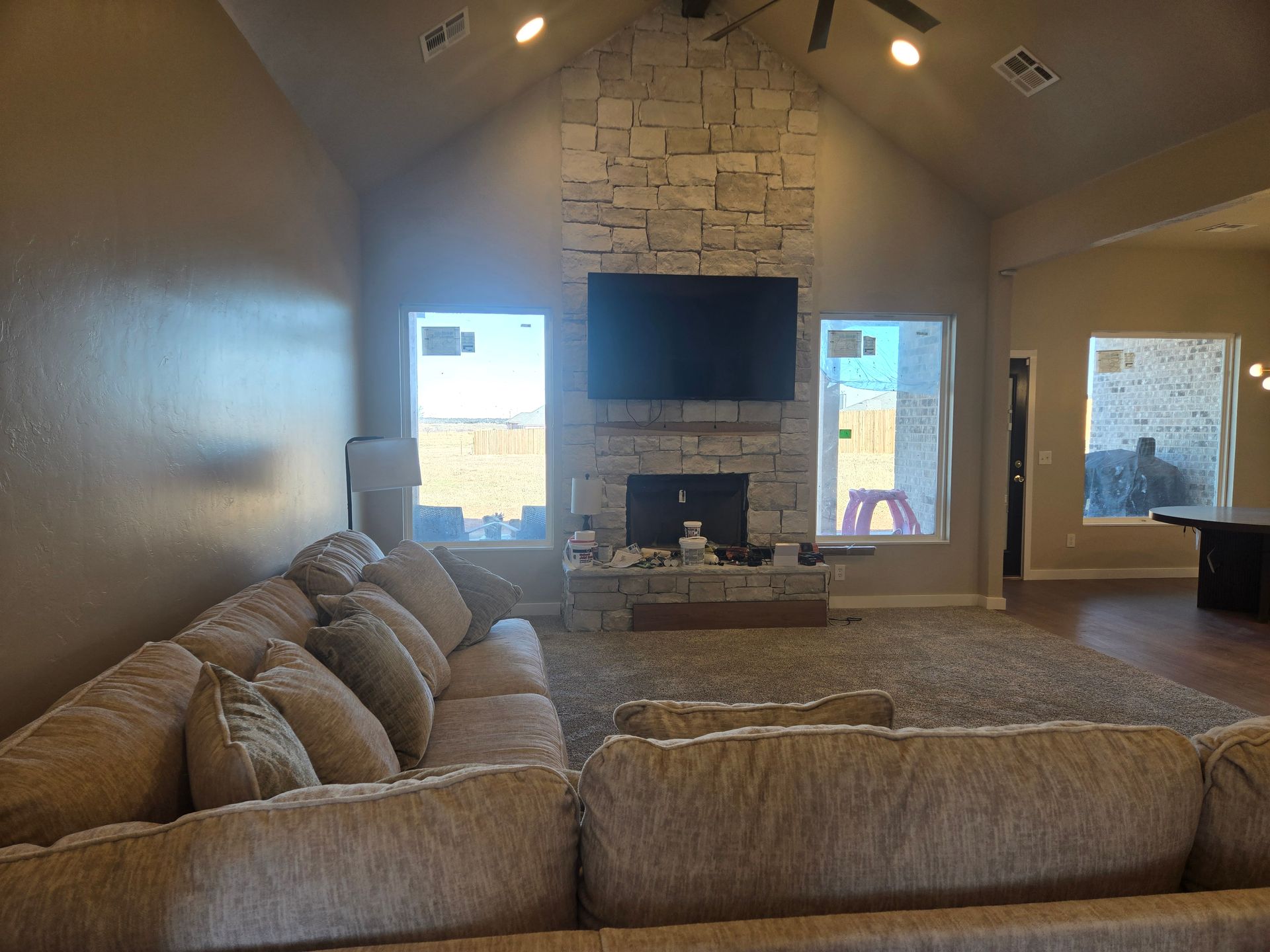Cozy living room with beige sectional, stone fireplace, wall-mounted TV, and large windows