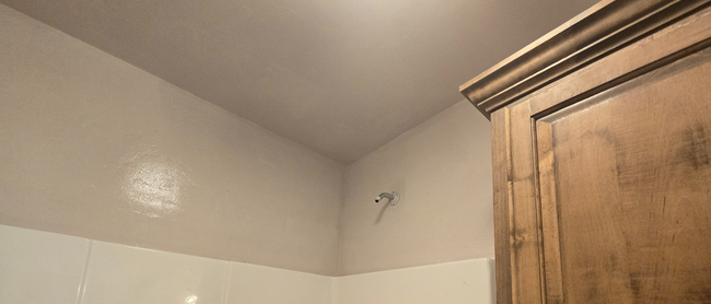 Bathroom corner with white tile walls, a showerhead, and a wooden cabinet on the right.