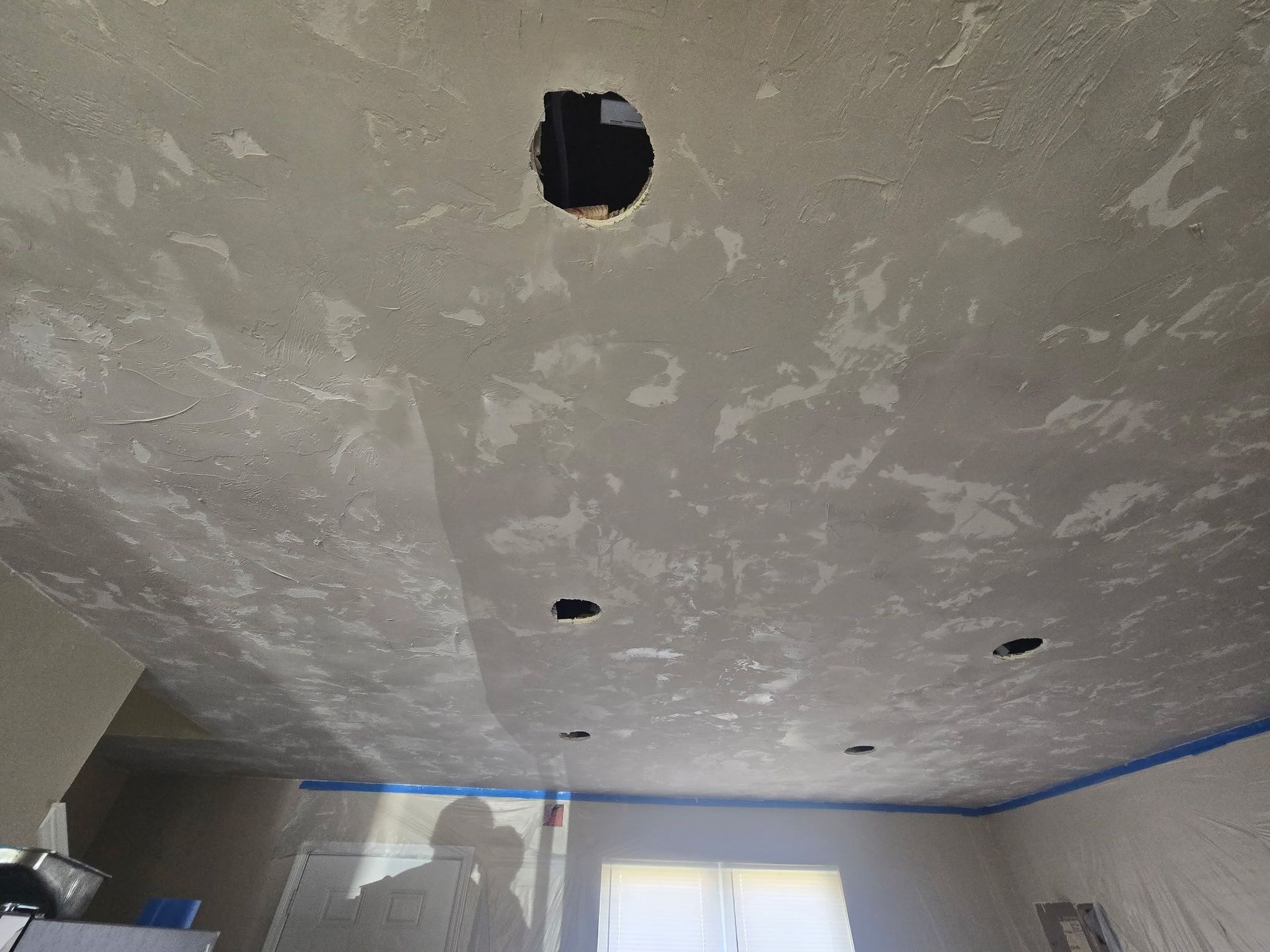 Unfinished ceiling with several cutouts and blue painter’s tape along the top of the walls.