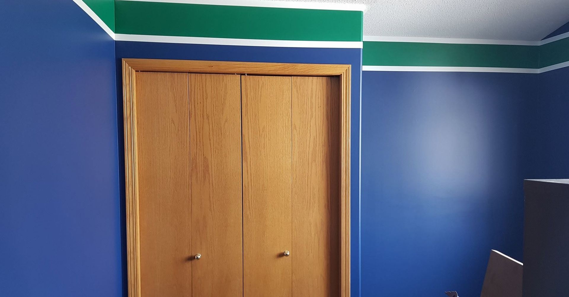 Blue room with wooden closet doors and green-and-white trim along the ceiling.