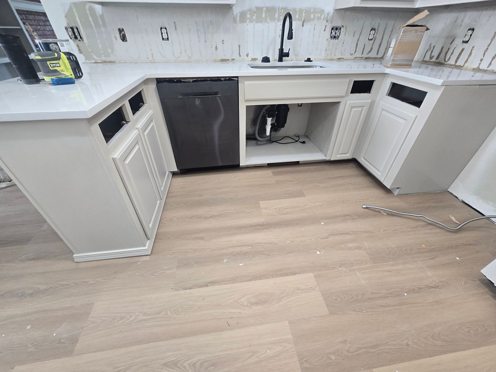 Modern white kitchen with black dishwasher, sink, cabinets, and light wood floor, cabinet under sink open