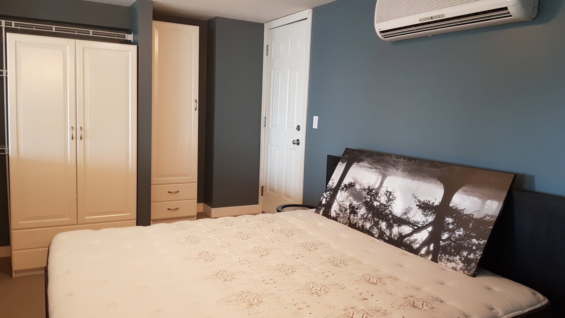 Bedroom with a bed, wardrobe, wall mirror, and air conditioner on a blue-gray wall.