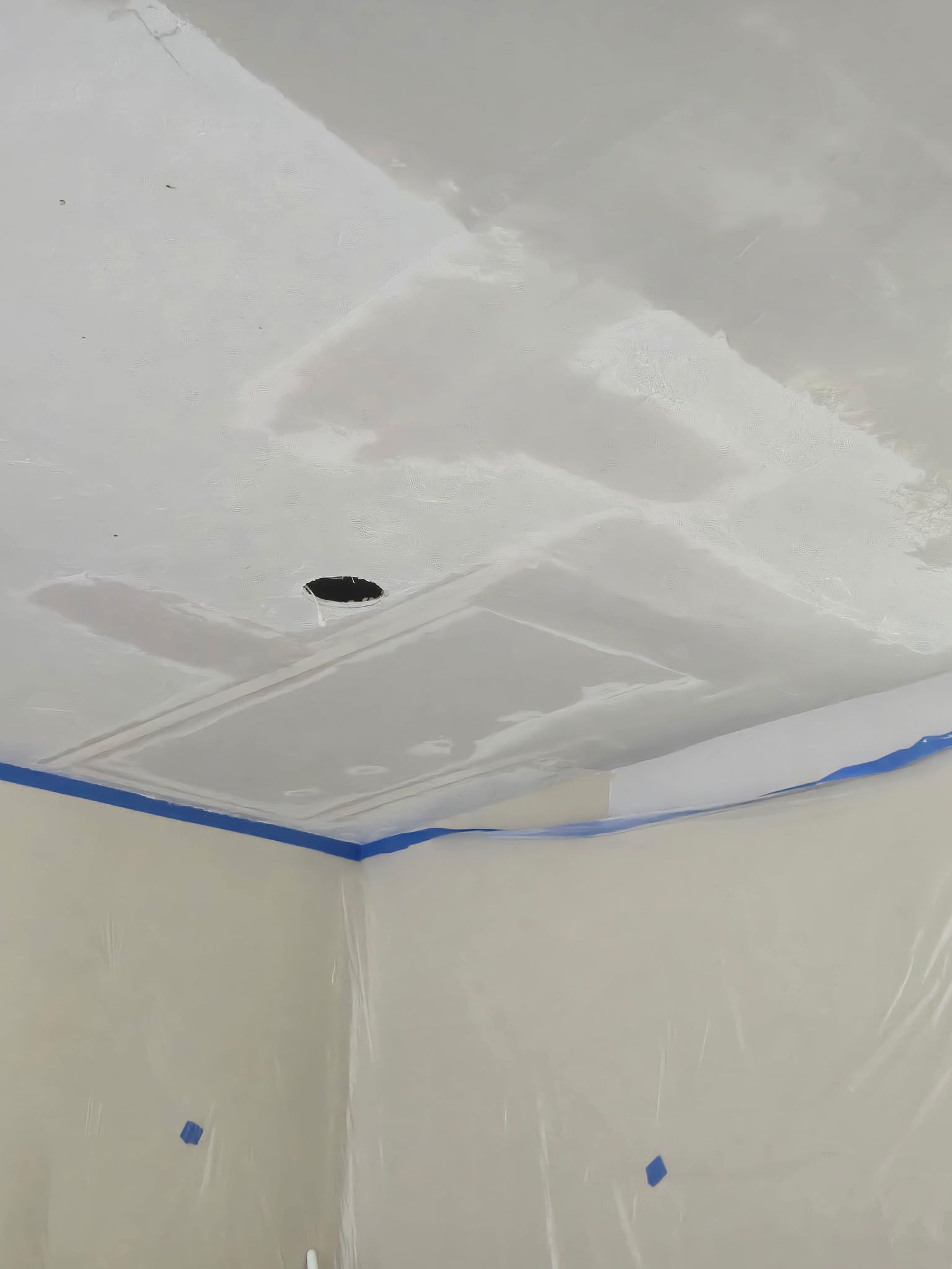 Ceiling with patched drywall, a small hole, and blue painter’s tape along the walls