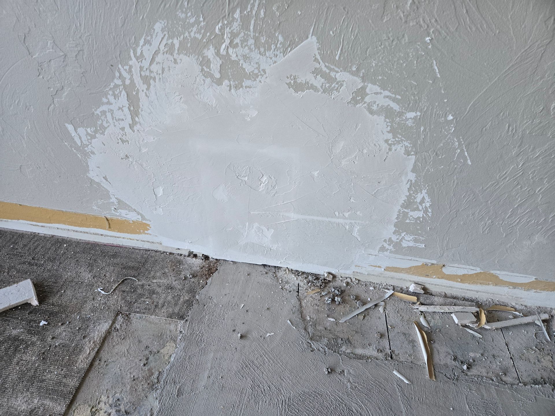 Damaged interior wall with peeling white plaster above a rough concrete floor