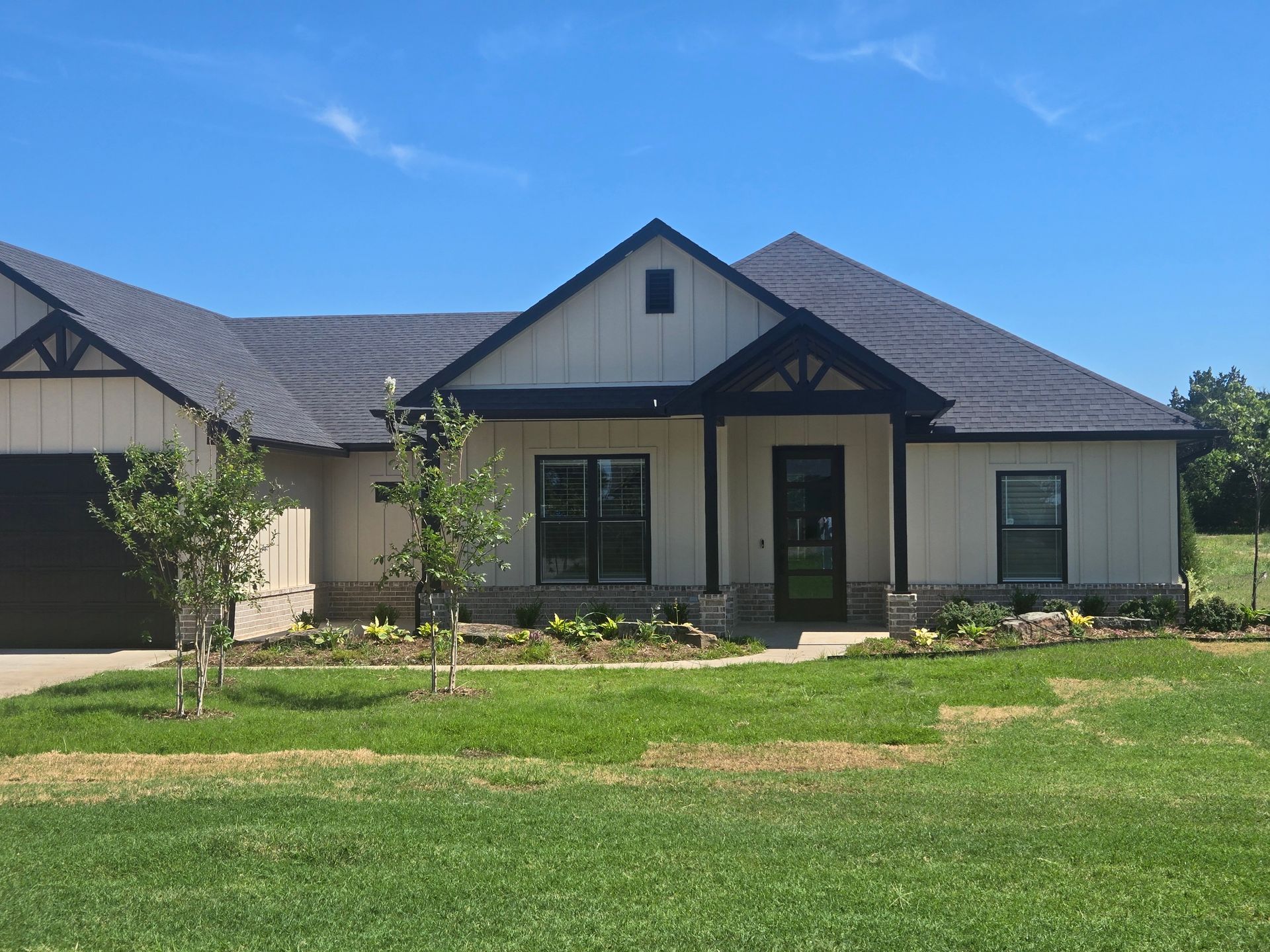 Single-story beige house with dark roof and a green lawn under a blue sky