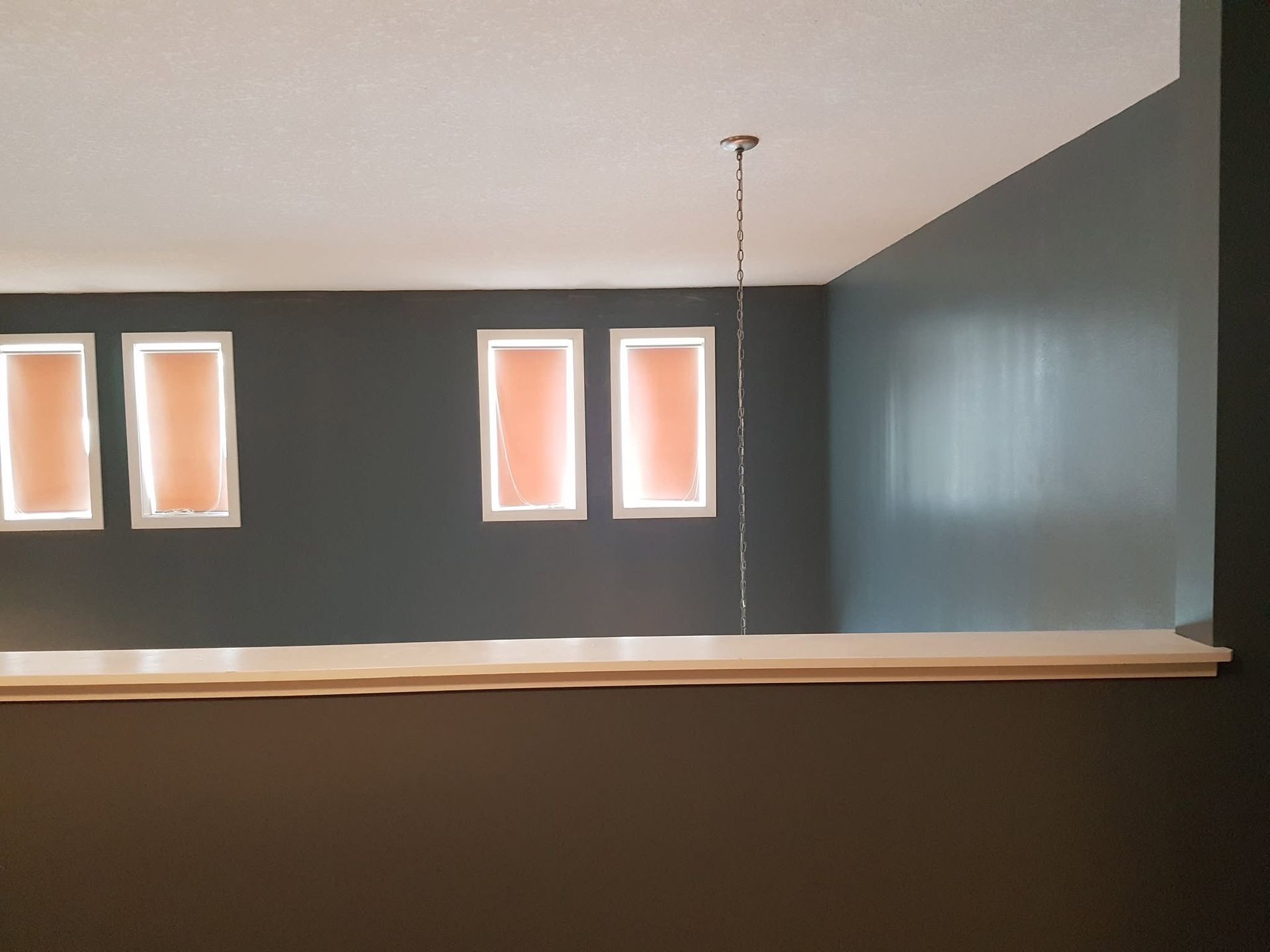 Minimalist room with dark gray walls, small windows, and a hanging chain in the center.