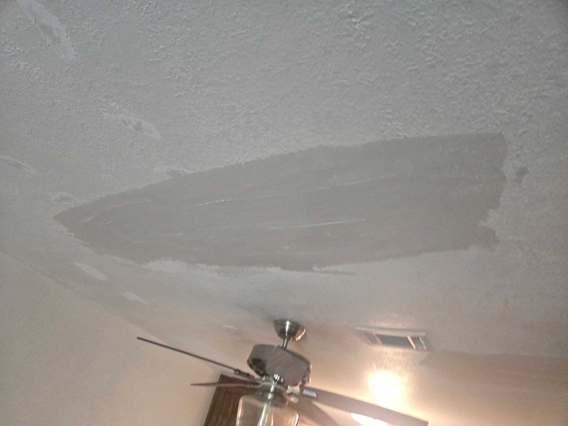 Ceiling with a large gray water stain above a ceiling fan and light fixture