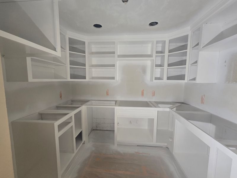 White unfinished kitchen with open cabinets, gray countertops, and a centered sink under recessed lights.
