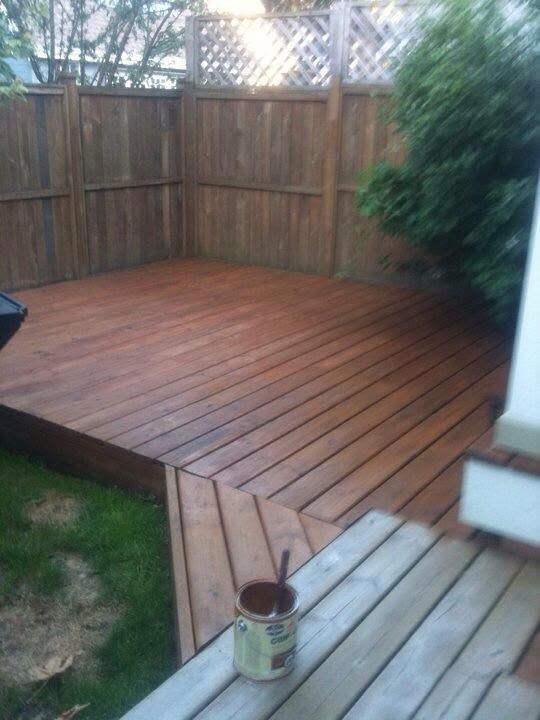 Wooden backyard deck with stepped edge, surrounded by a fence and grass, with a paint can in the foreground