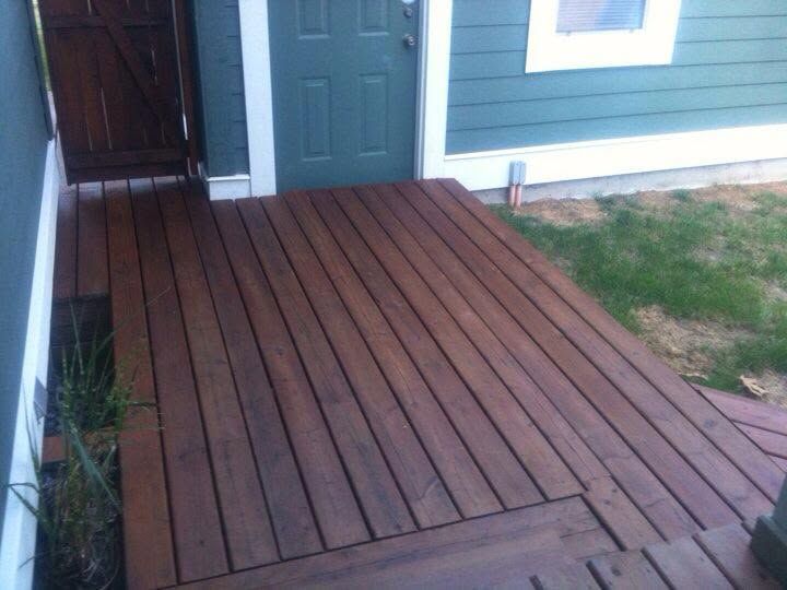 Wooden deck leading to a green front door beside a blue house and patchy lawn
