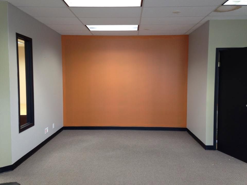 Empty office room with orange accent wall, gray carpet, and black doorways