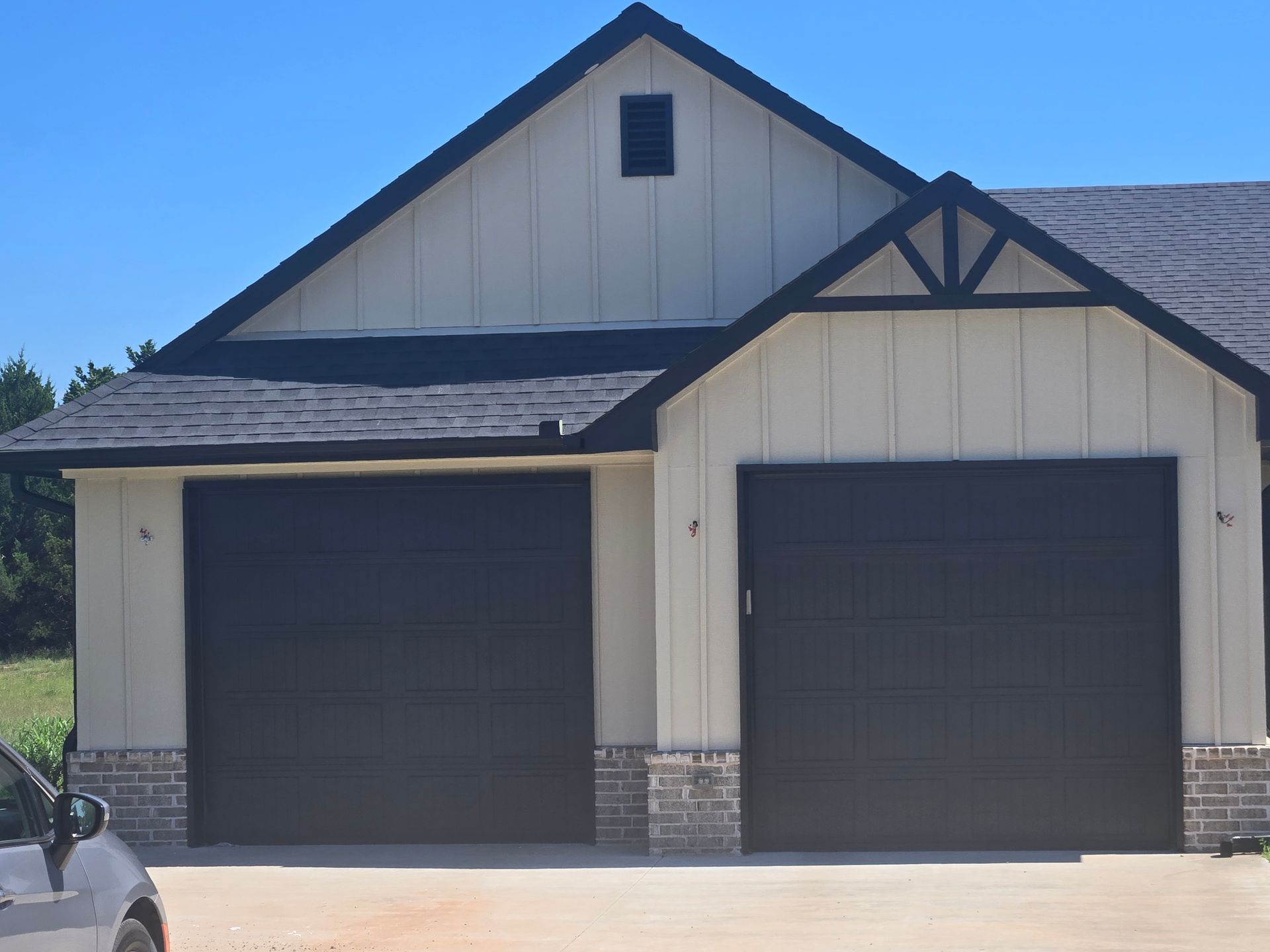 Two-car garage with beige siding, dark trim, and black doors under a gabled roof.