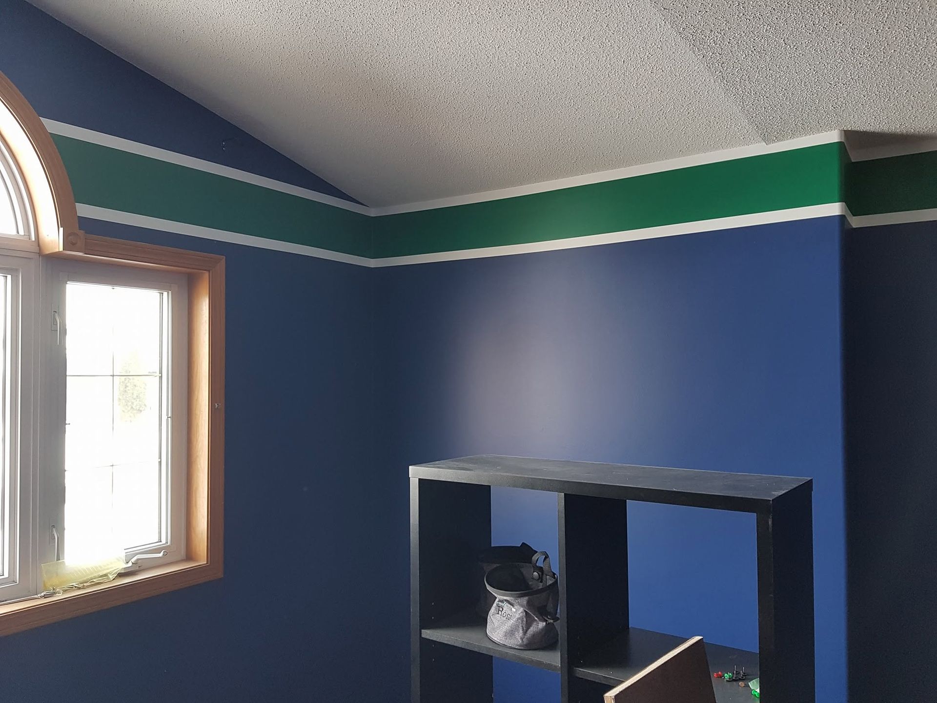 Blue bedroom corner with window, green-and-white trim, and black cubby shelf against the wall