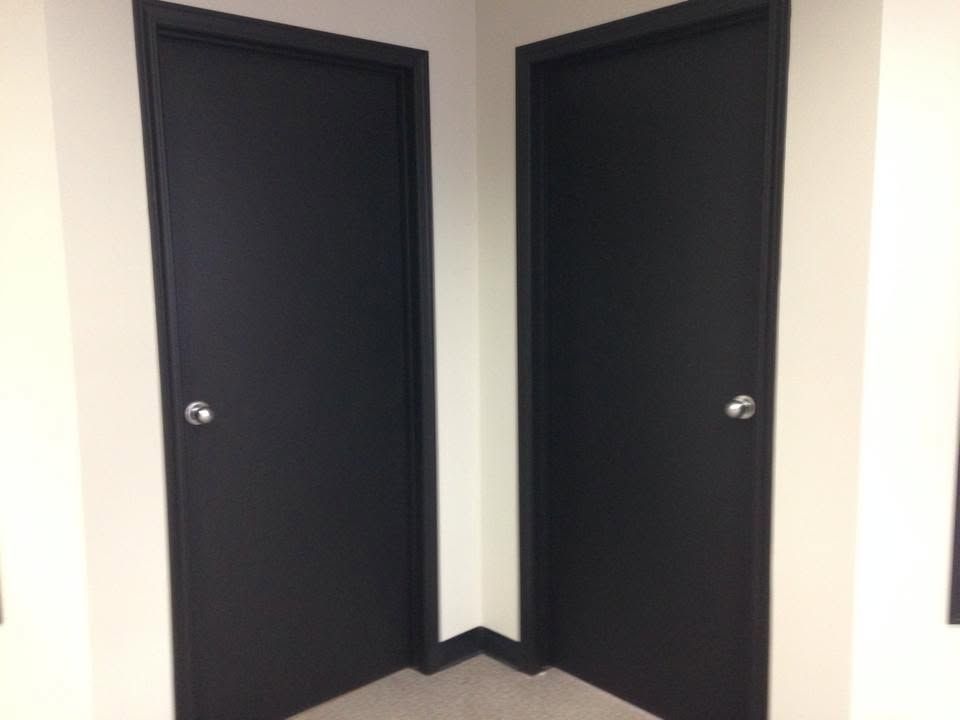 Two black doors in a corner of a white hallway with light wood floor