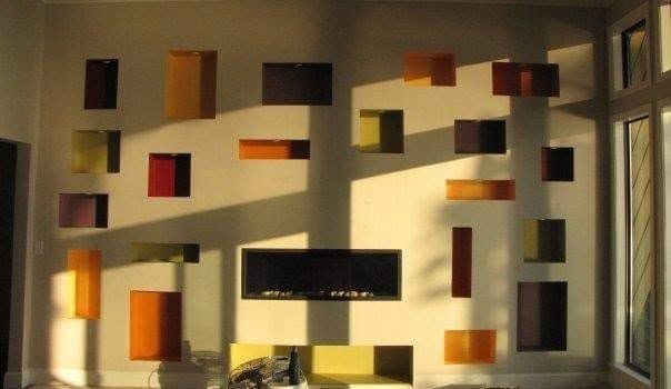 Sunlit wall with colorful geometric art panels and a central black shelf in a modern interior
