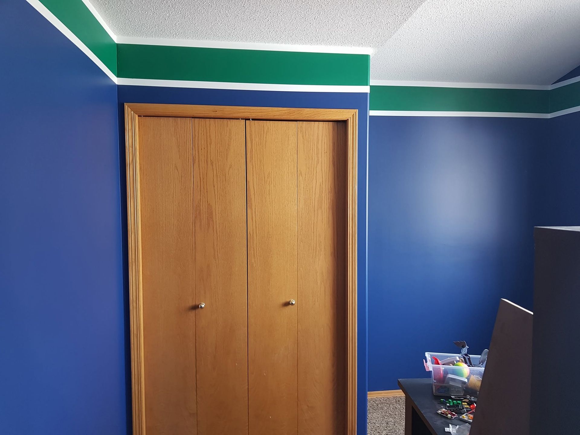 Blue bedroom wall with wooden closet doors and a dresser in the corner.
