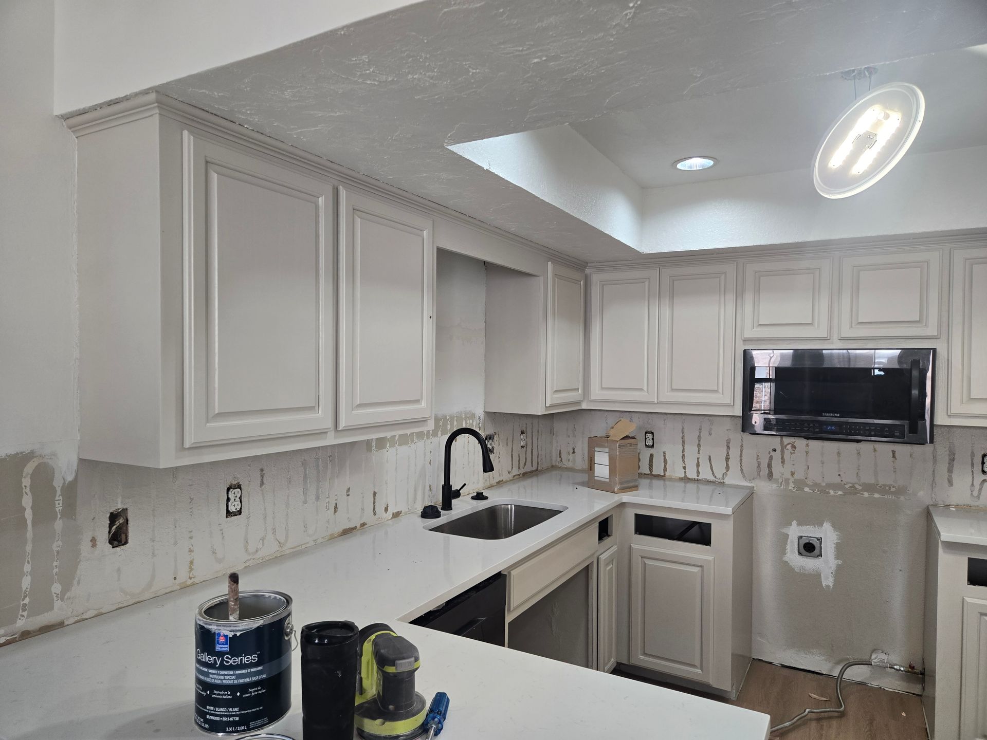 Partially renovated white kitchen with cabinets, counters, sink, and ceiling light installed