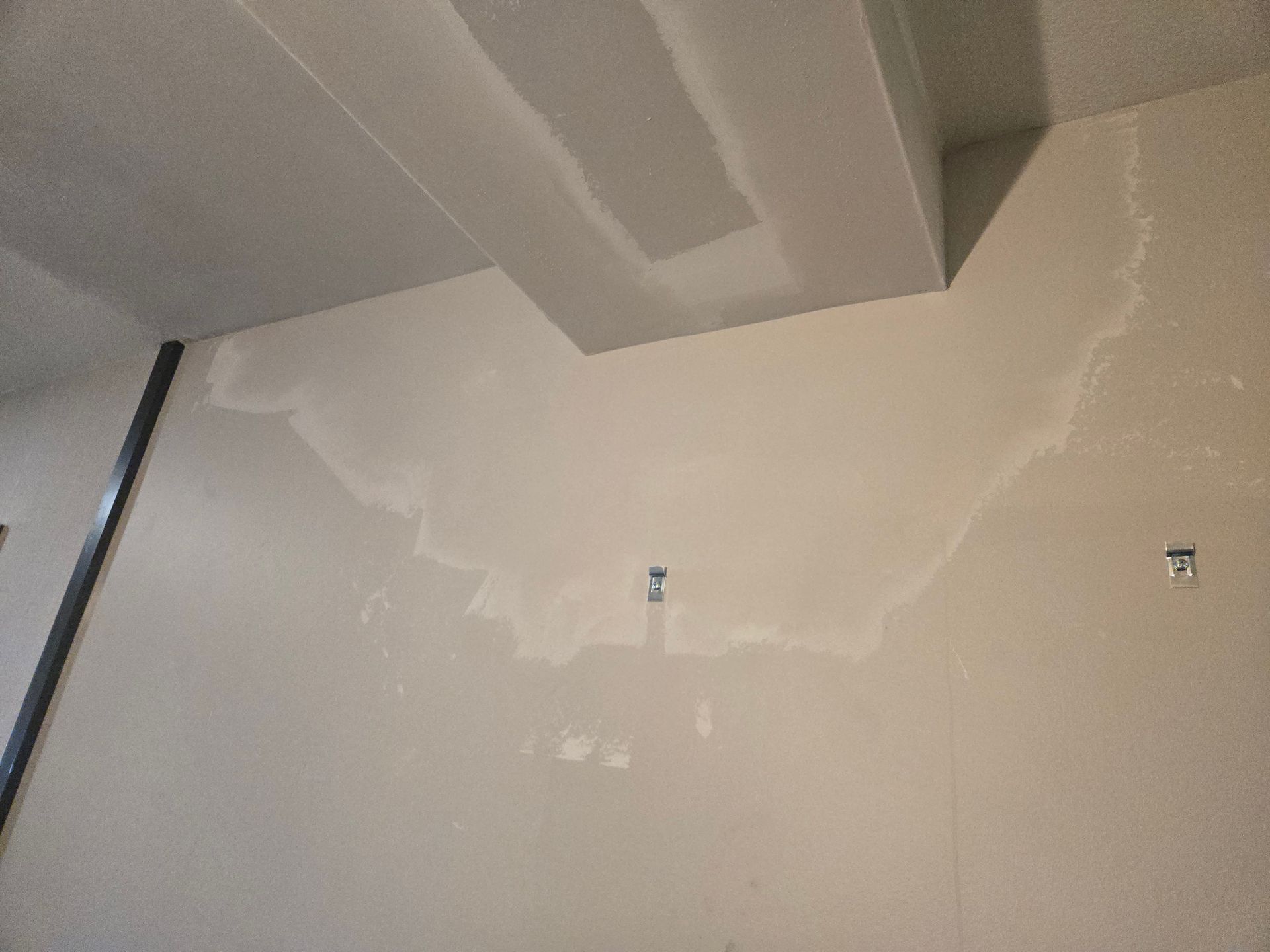 Beige interior wall with fresh plaster patches and exposed ceiling beam near the top.