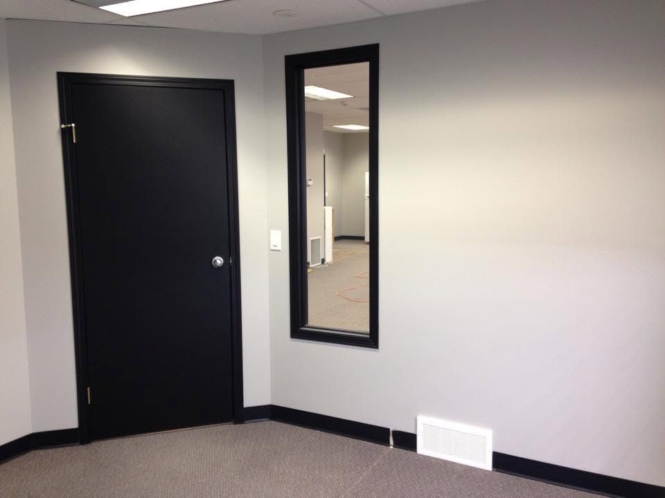 Empty room with black door, wall mirror, and white vent on gray walls