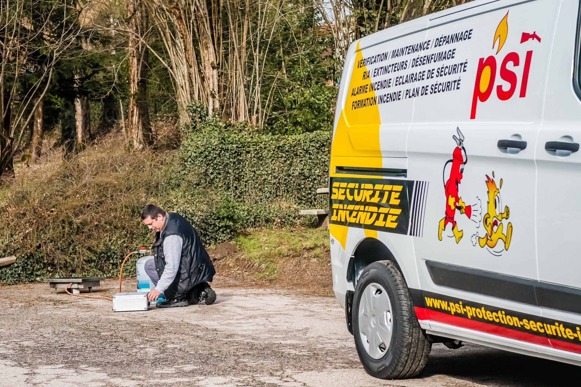 Un homme est agenouillé devant une camionnette blanche sur laquelle est écrit psi.