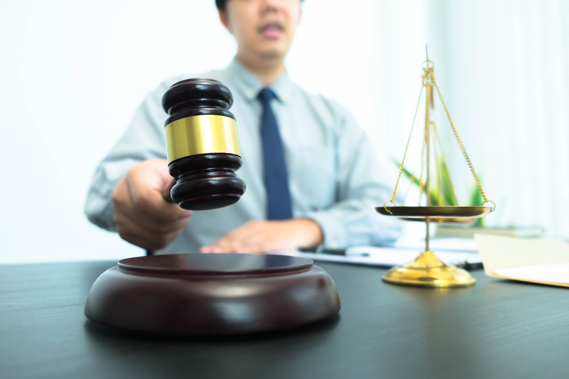 Judge’s gavel on desk with scales of justice; blurred lawyer in the background.