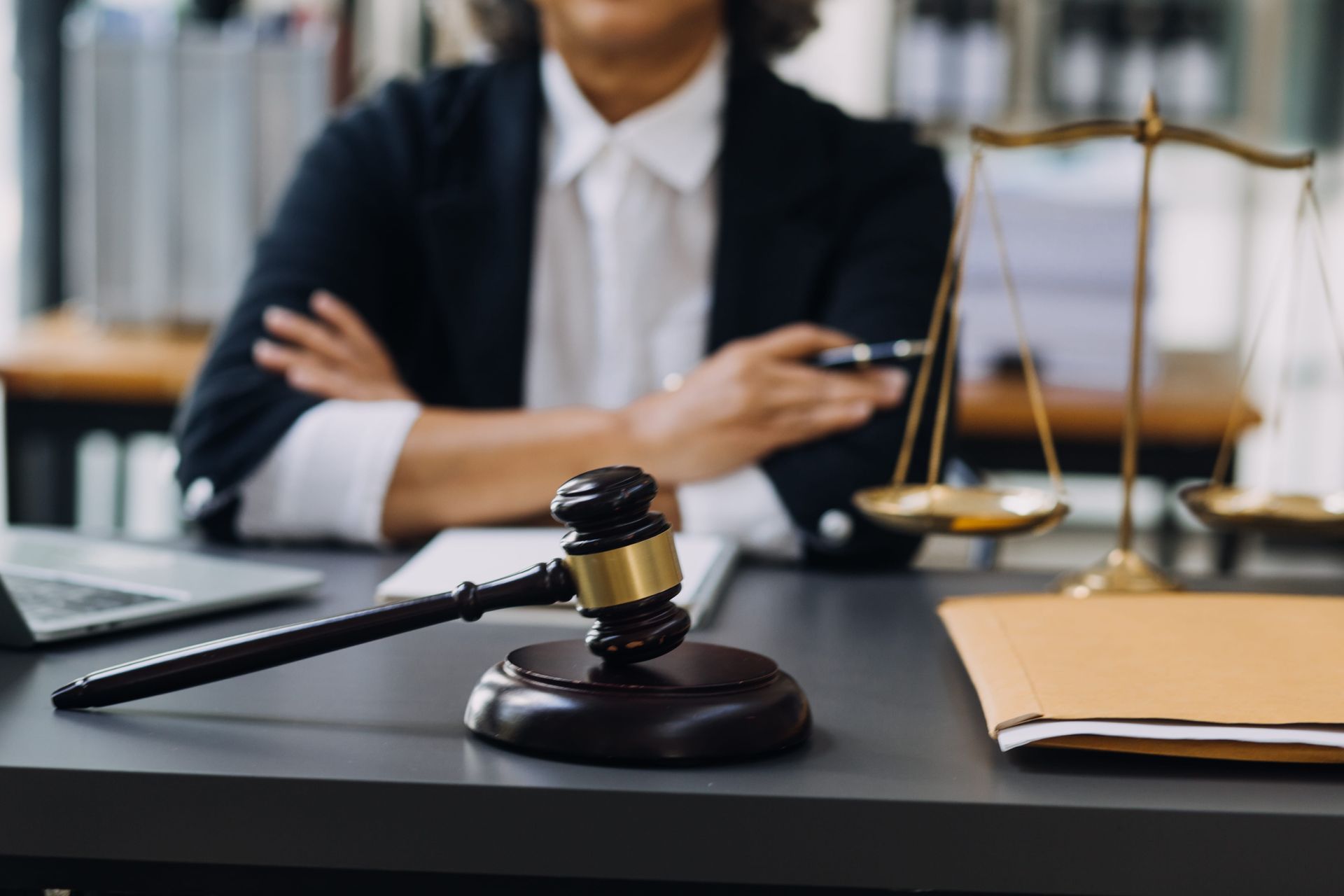 Lawyer seated behind desk with gavel, scales of justice, and laptop in a courtroom office