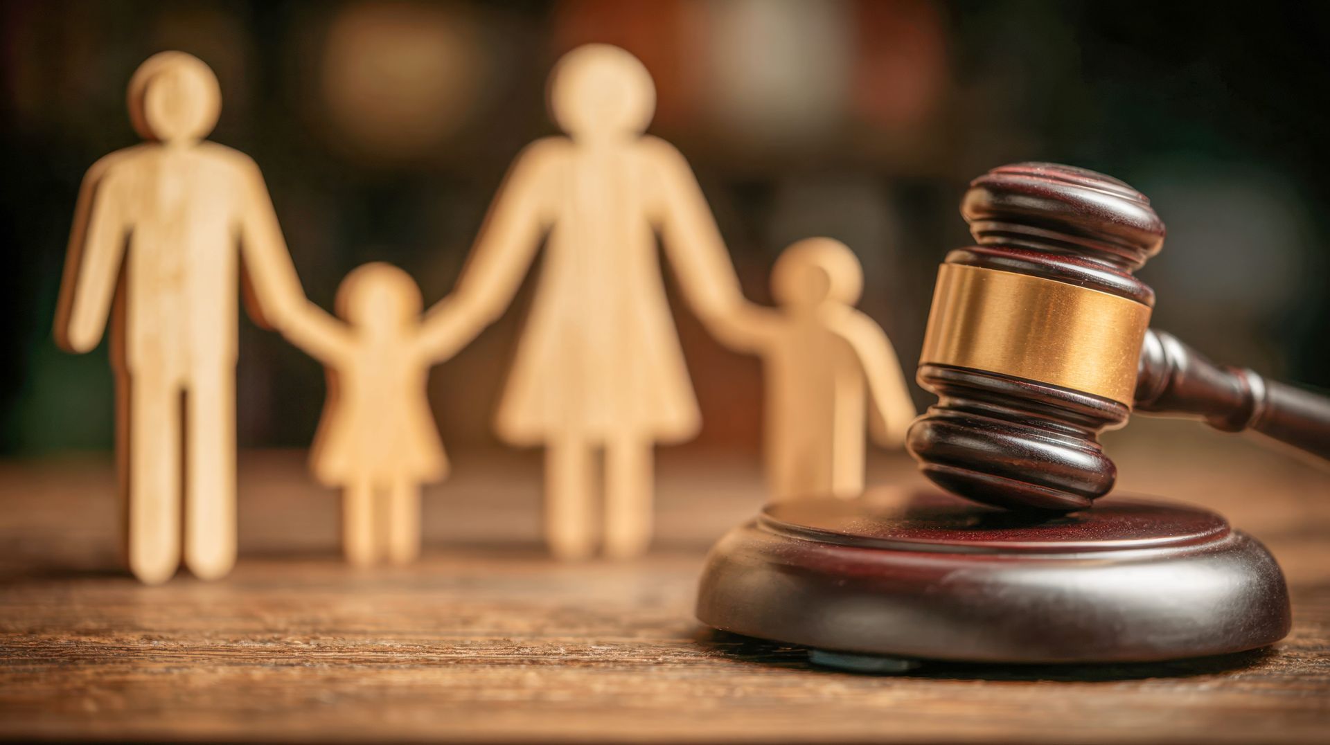 Wooden family figures beside a judge’s gavel on a table, symbolizing family law or custody.