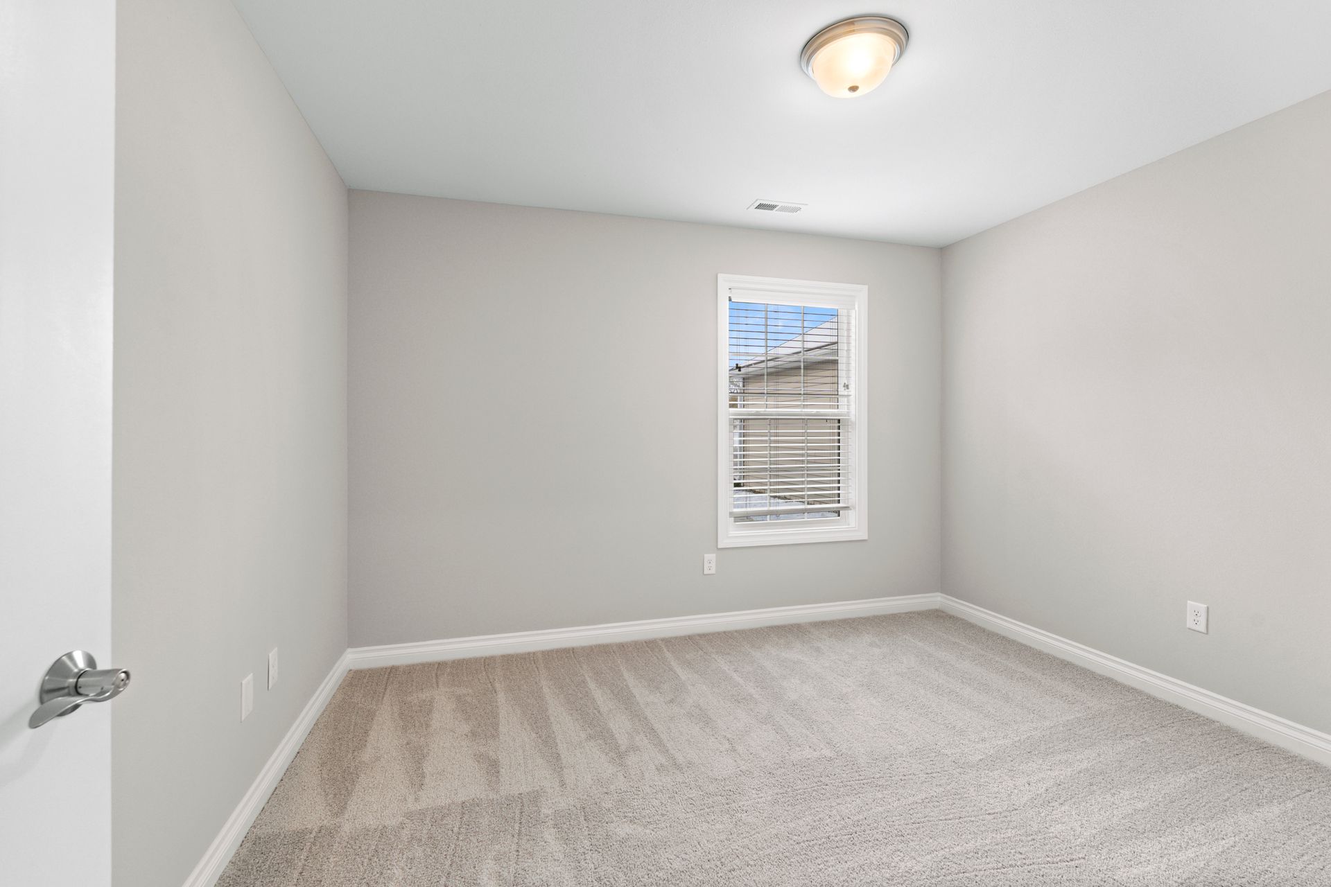 Empty bedroom with light gray walls, carpet, and a small window.